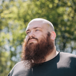 A portrait of myself. Bearded, bald, male white middle-aged person in front of some trees.